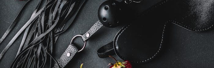 A stylish flat lay of leather BDSM accessories with fresh strawberries on a dark background.